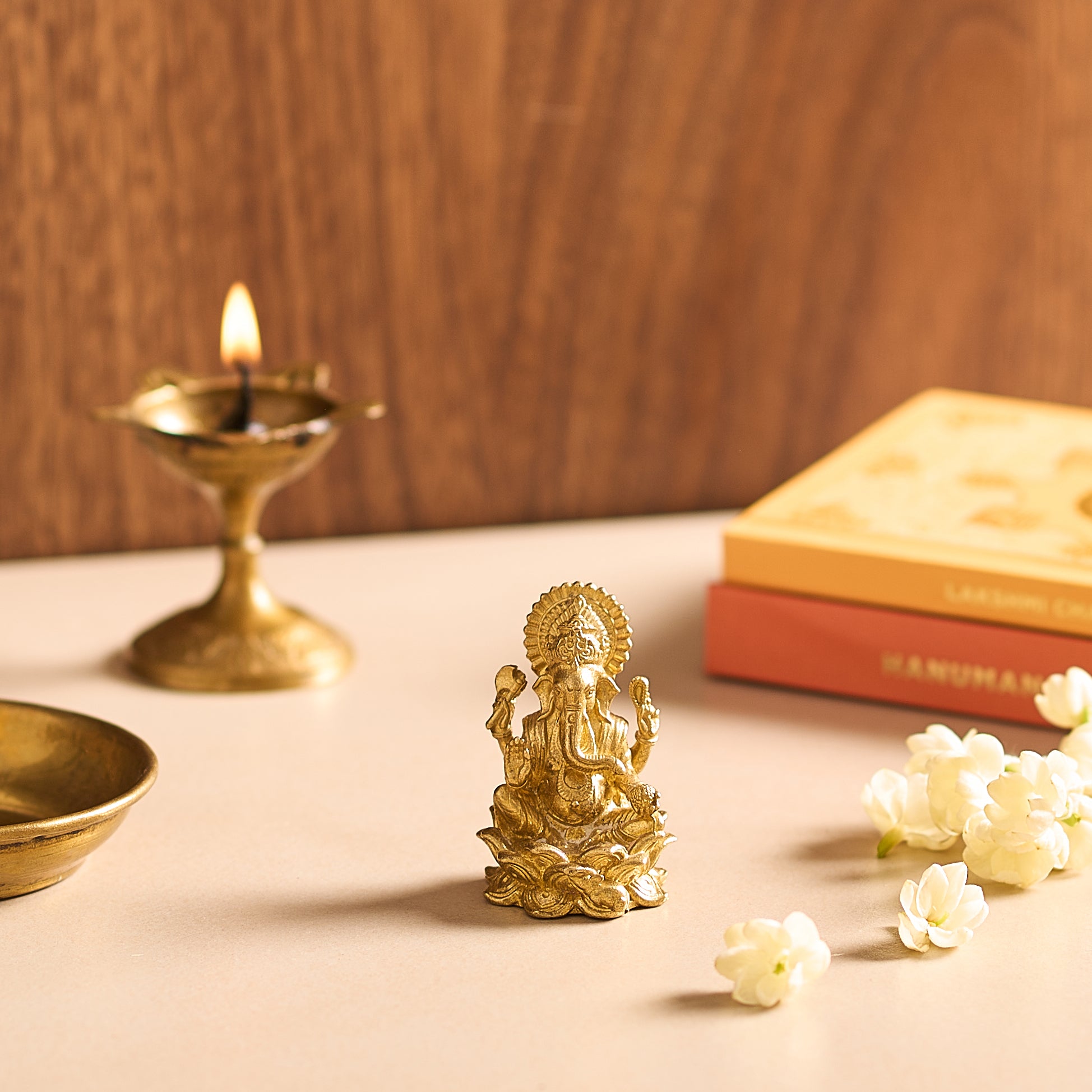 Gold-colored statue of a deity on a table with a lit candle and flowers.
