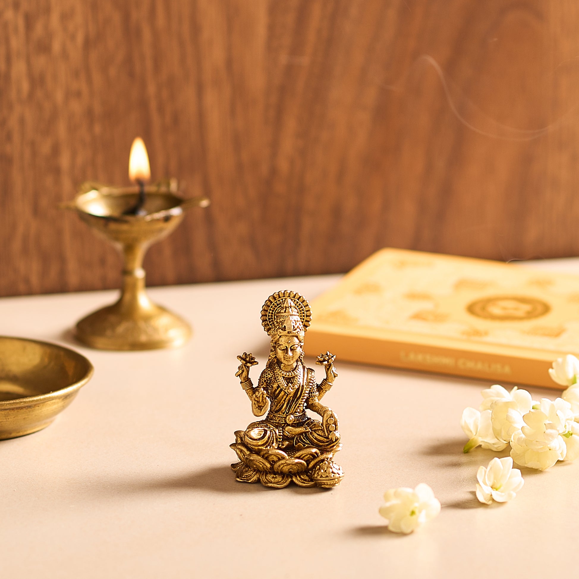 Bronze statue of a deity on a table with a lit candle and flowers.
