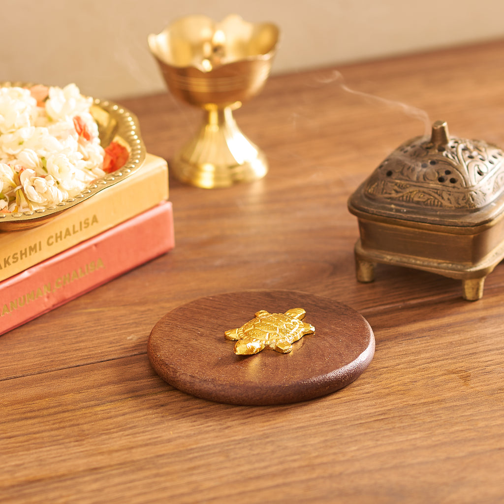 Wooden coaster with a gold turtle design on a wooden surface with decorative items.