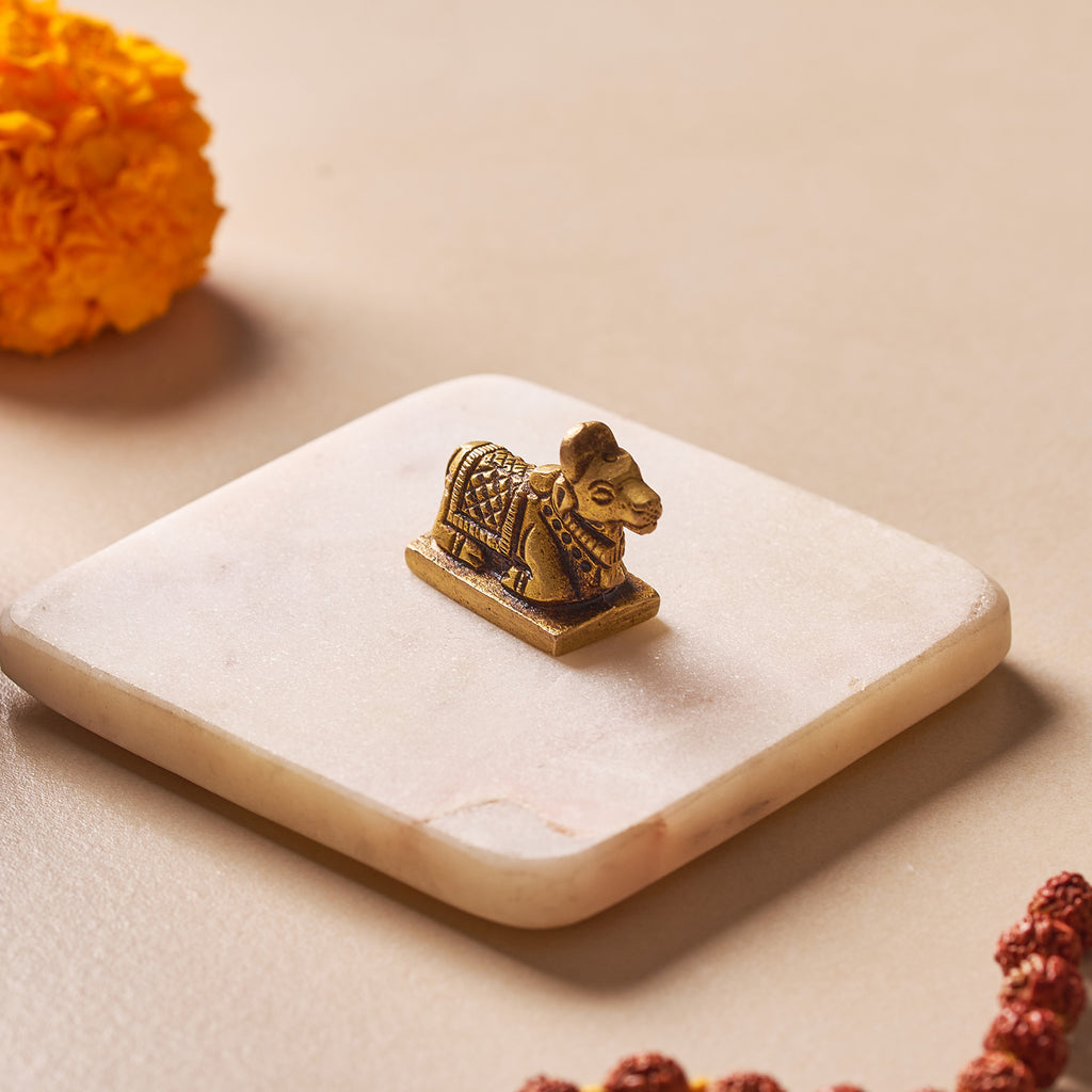 Bronze lion statue on a white stone surface with marigold flowers and beads in the background