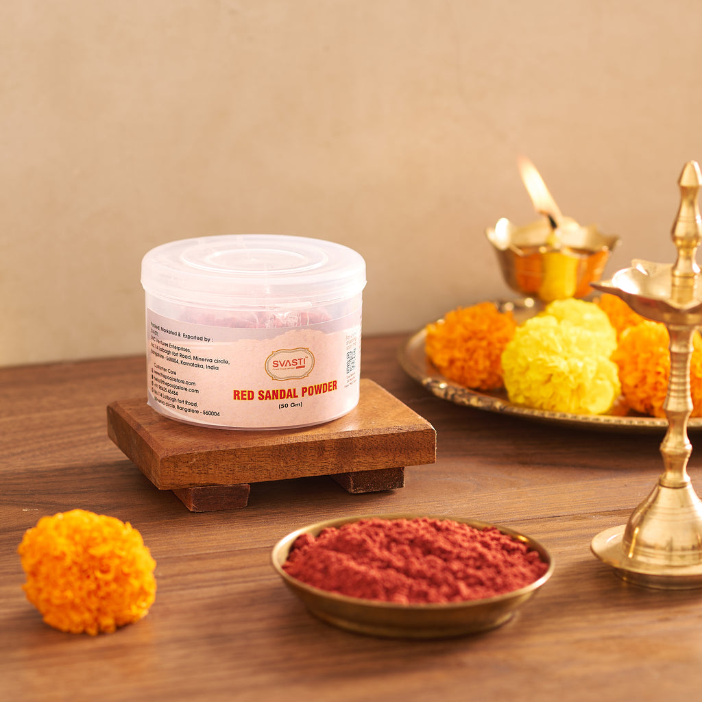 Container of red sandalwood powder on a wooden platform with marigold flowers and religious offerings in the background.