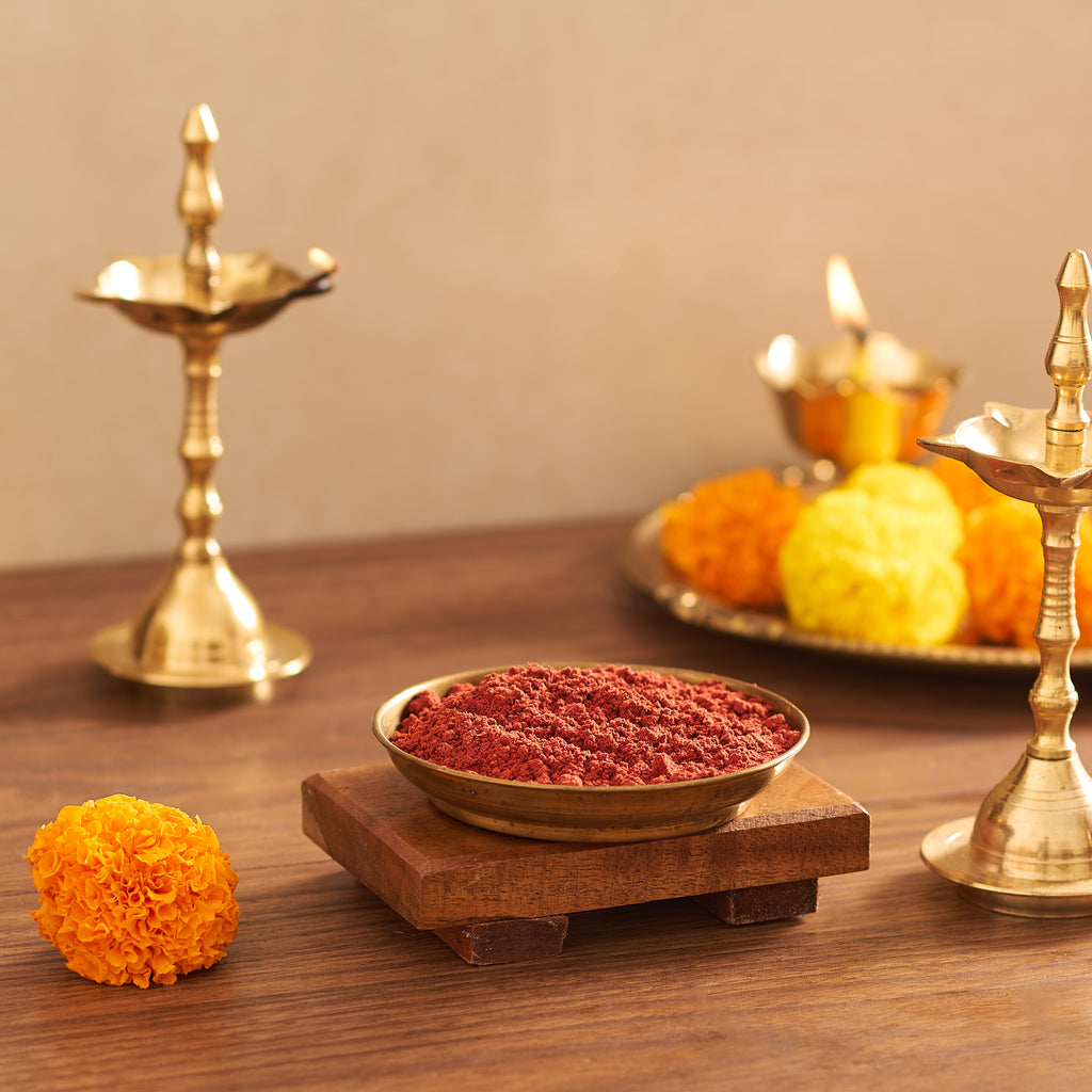 Decorative setup with red powder, marigold flowers, and brass lamps on a wooden surface.
