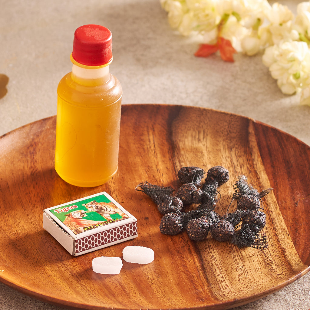 Bottle of yellow liquid, matchbox, and dried fruits on a wooden plate with flowers in the background.
