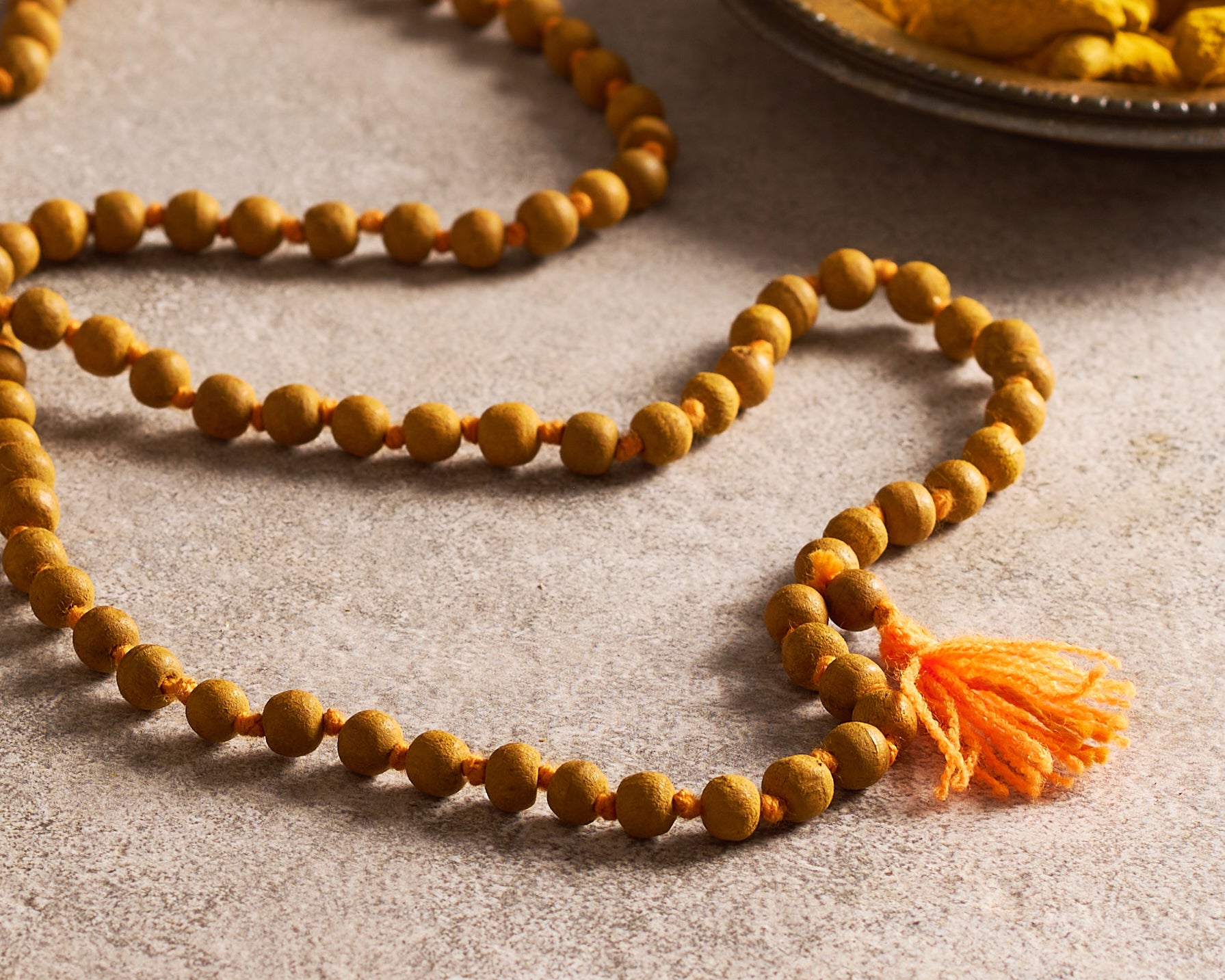 Orange beaded necklace with a tassel on a textured surface