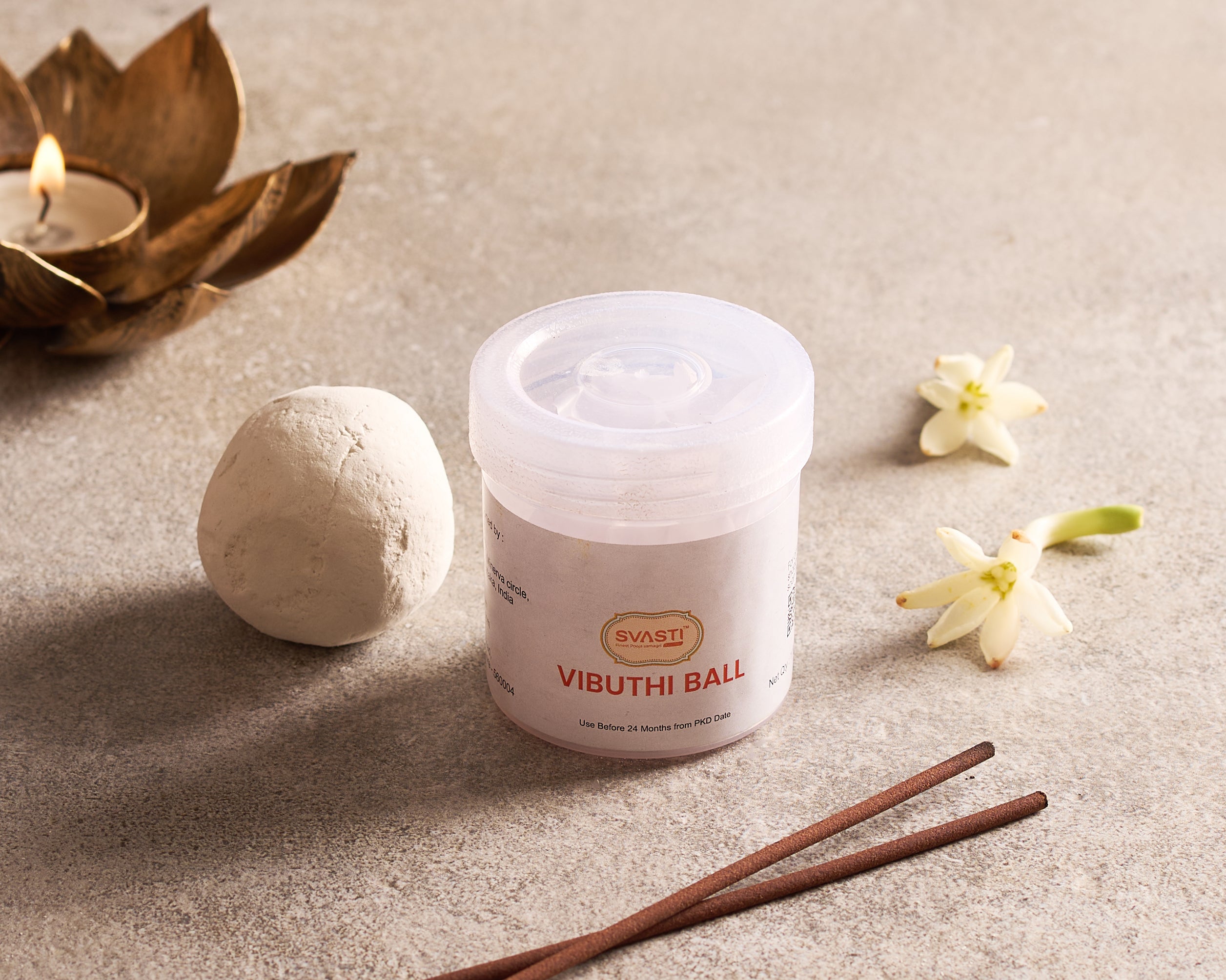 Vibhuti ball container with a ball, incense sticks, and flowers on a neutral background