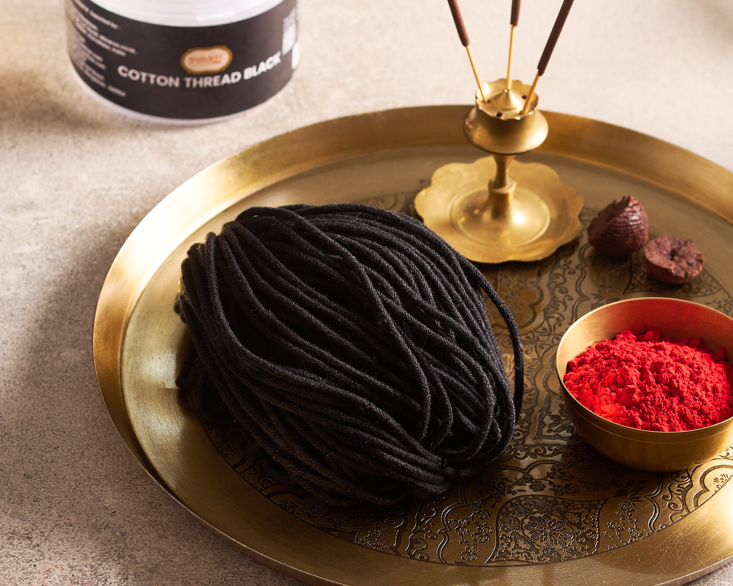 Black cotton thread on a gold tray with red powder and a bottle of cotton thread.