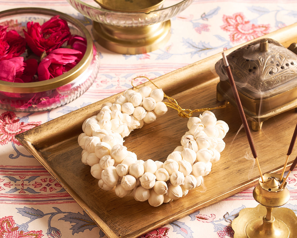 Decorative white beaded necklace on a wooden tray with incense sticks and flowers.