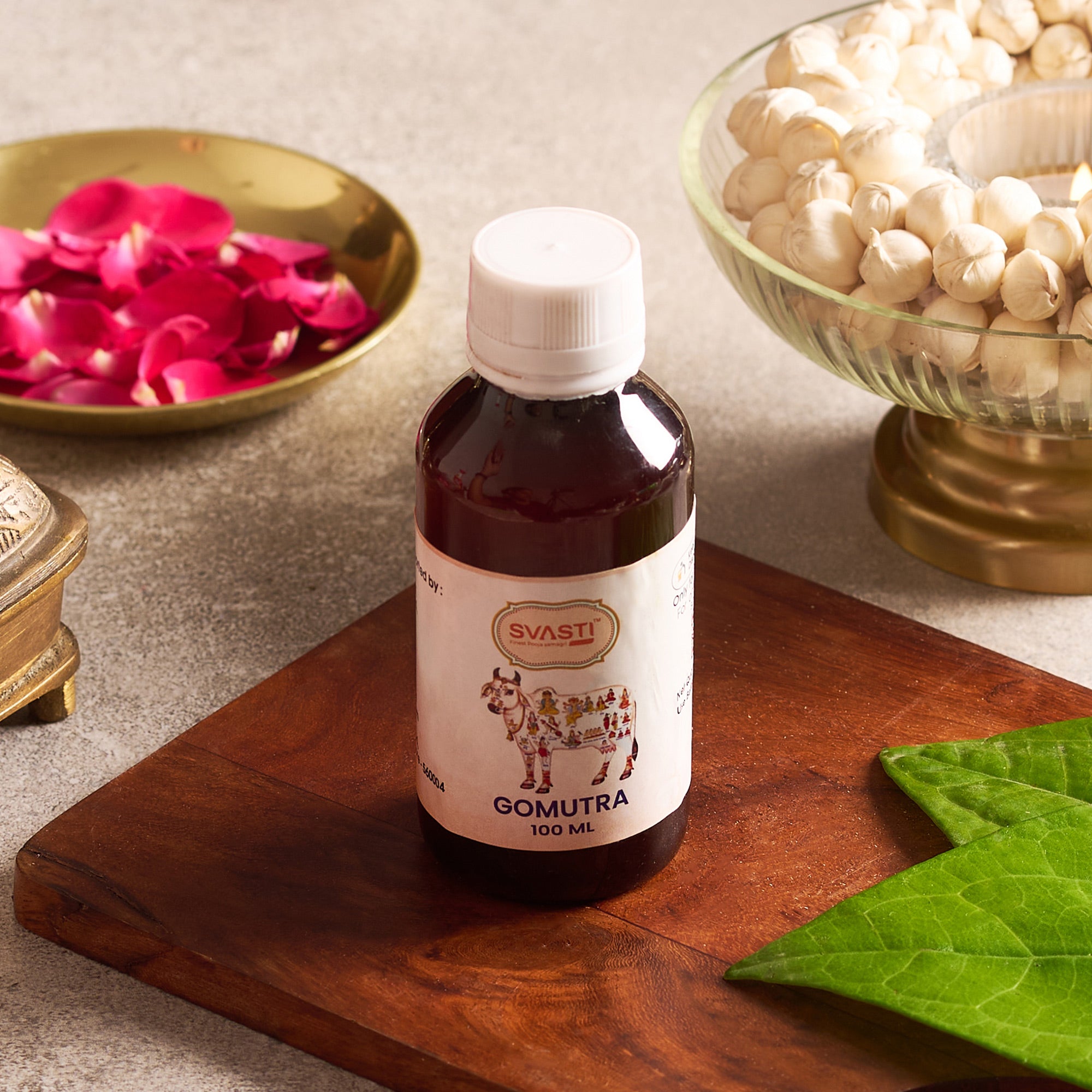 Bottle of Svasti Gomutra on a wooden surface with decorative elements.