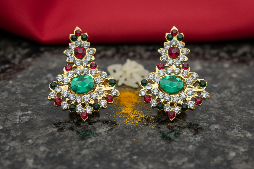 A pair of earrings with red and green stones set in gold-colored metal casing, designed for use in religious ceremonies.