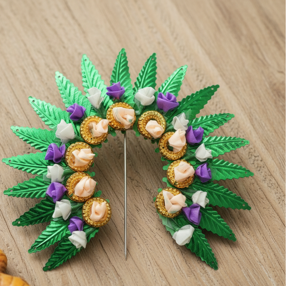 A decorative brooch or pin shaped like a leafy wreath, featuring metallic green leaves, peach and white paper flowers, and purple accents, with a silver pin stem in the center, shown on a dark gray gradient background.