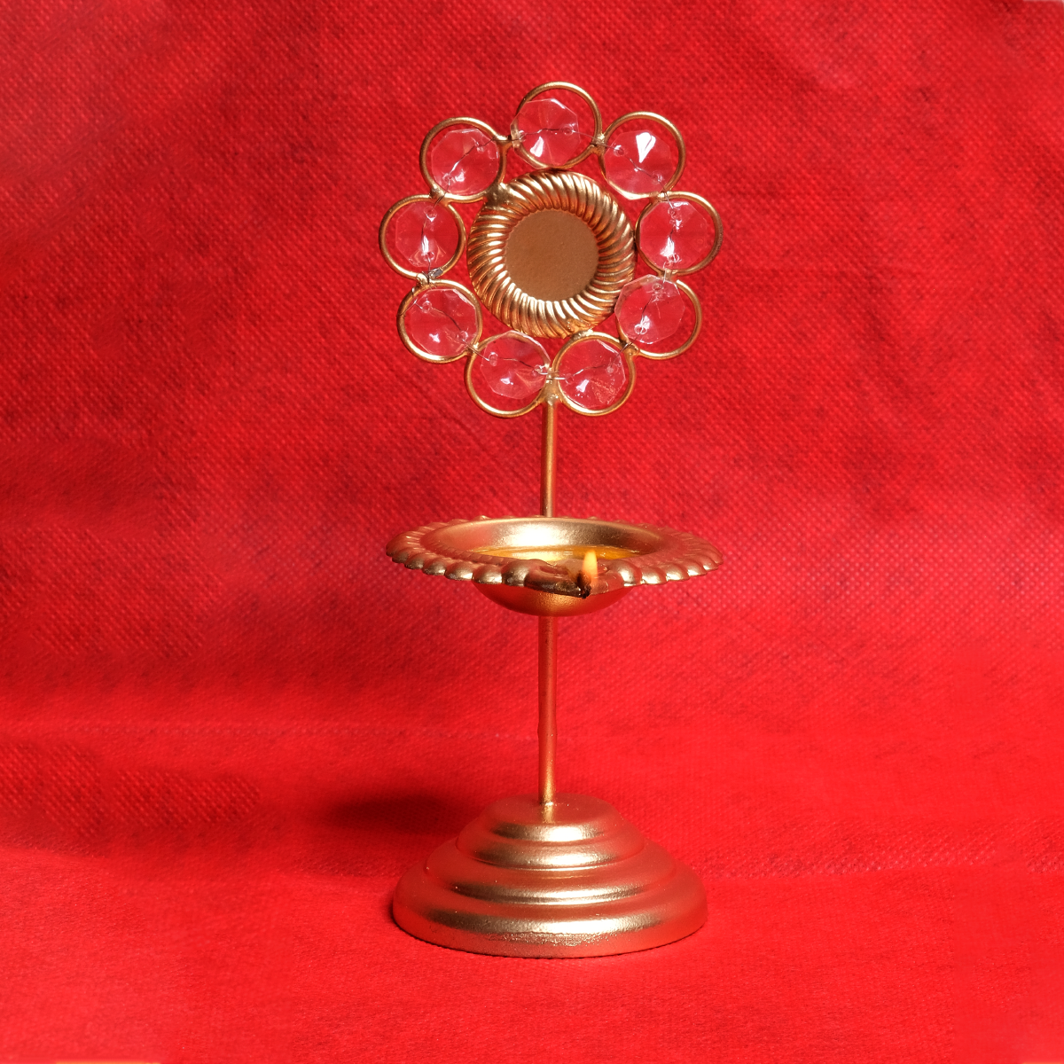 A gold-colored crystal diya with a floral design on a red background