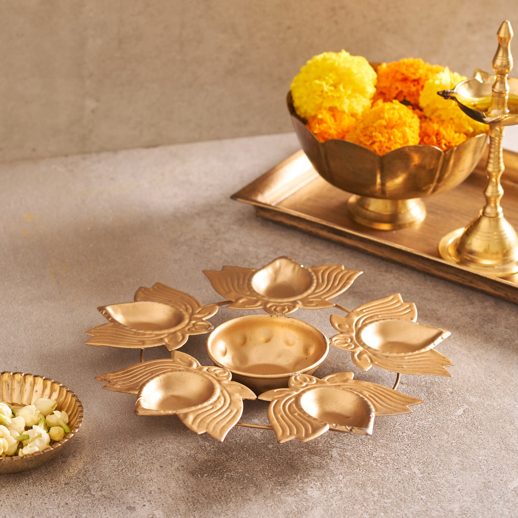 Decorative gold lotus-shaped diya with marigold flowers on a neutral background