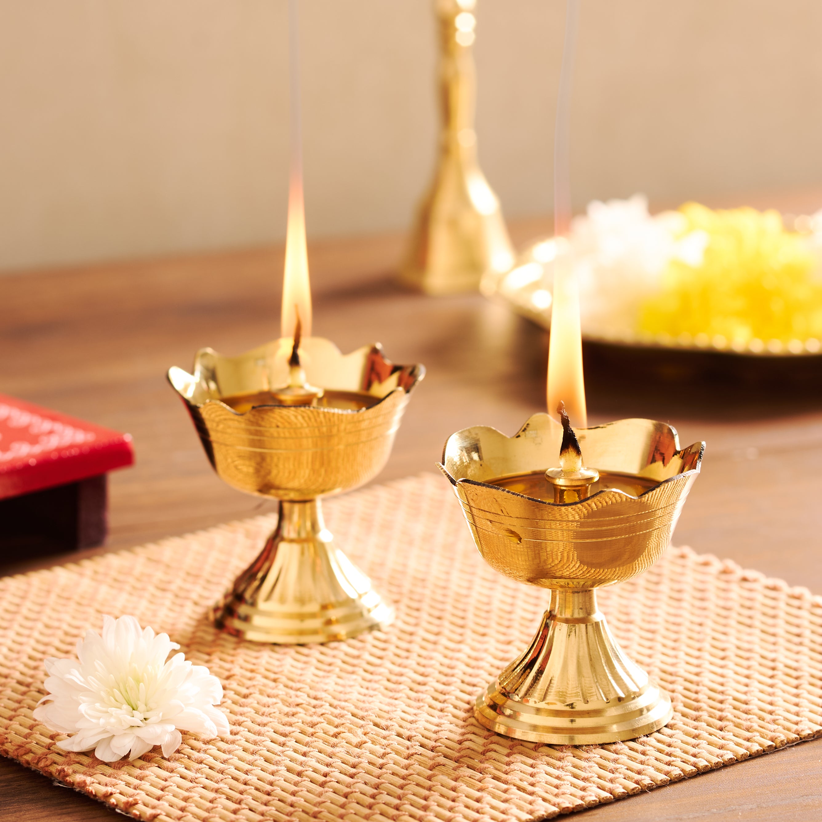 Two lit gold oil lamps on a woven mat with a blurred background