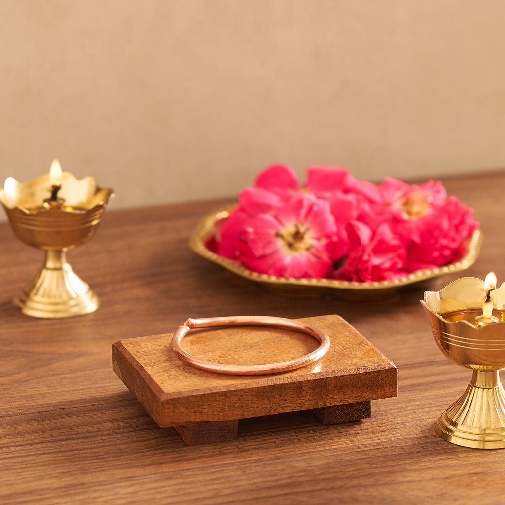 Decorative setup with pink flowers, a wooden tray, and gold lamps on a wooden surface.