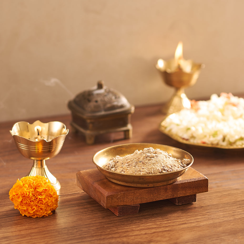 Traditional offering with brass bowl, incense, and flowers on a wooden surface.