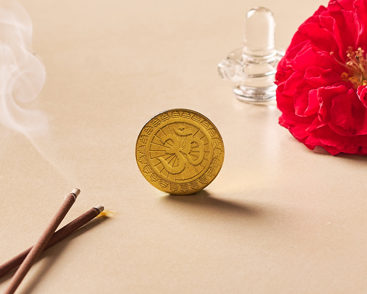 Gold coin with astrological design on a beige surface with a red flower and candles.