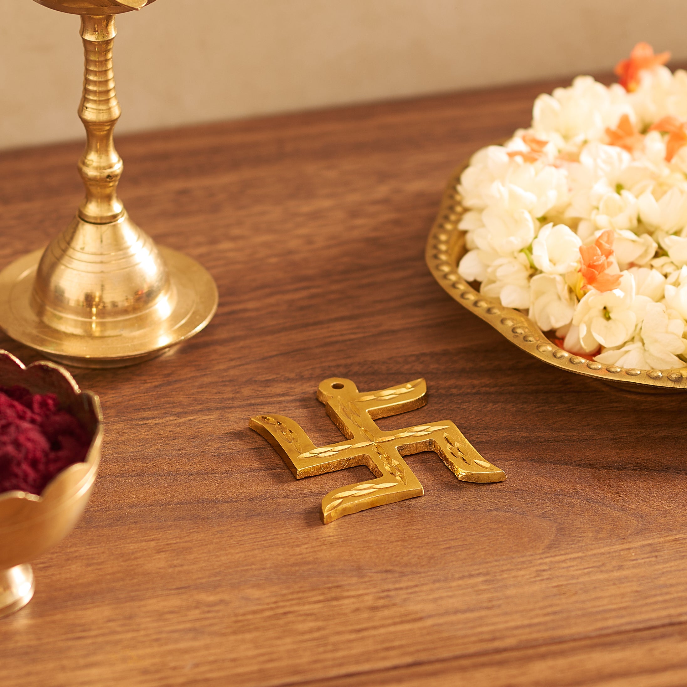 Gold swastika symbol on a wooden surface with floral offerings and a brass lamp.