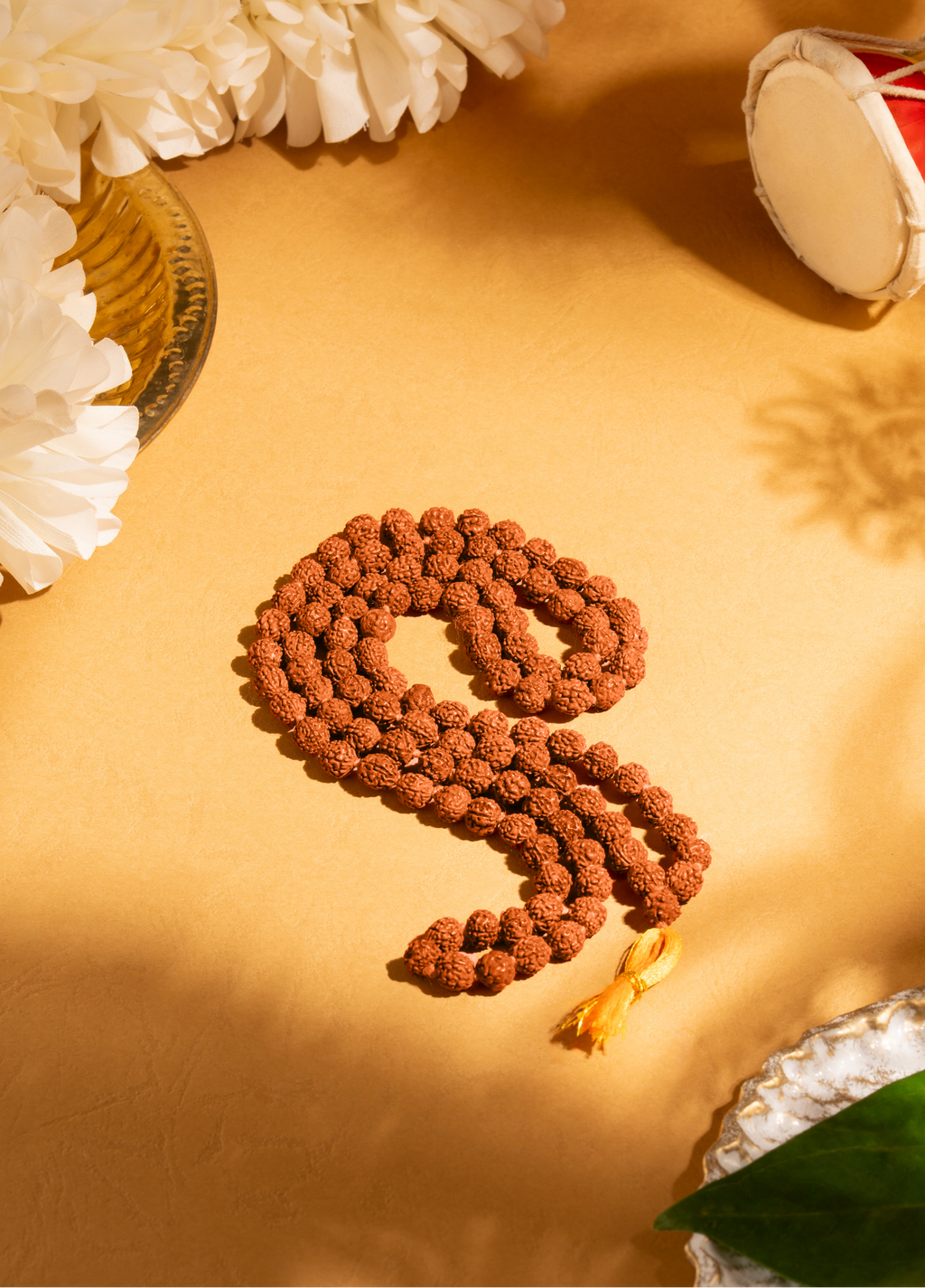 Top-down view of the textured brown rudraksha mala coiled gracefully next to its branded terracotta-colored packaging box.
