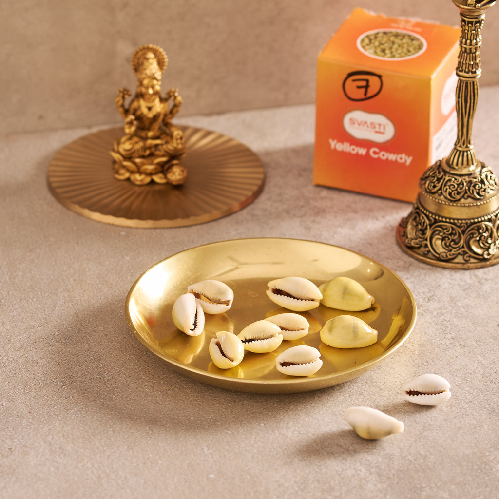 Gold plate with cowrie shells, small statue, and bell on a beige surface