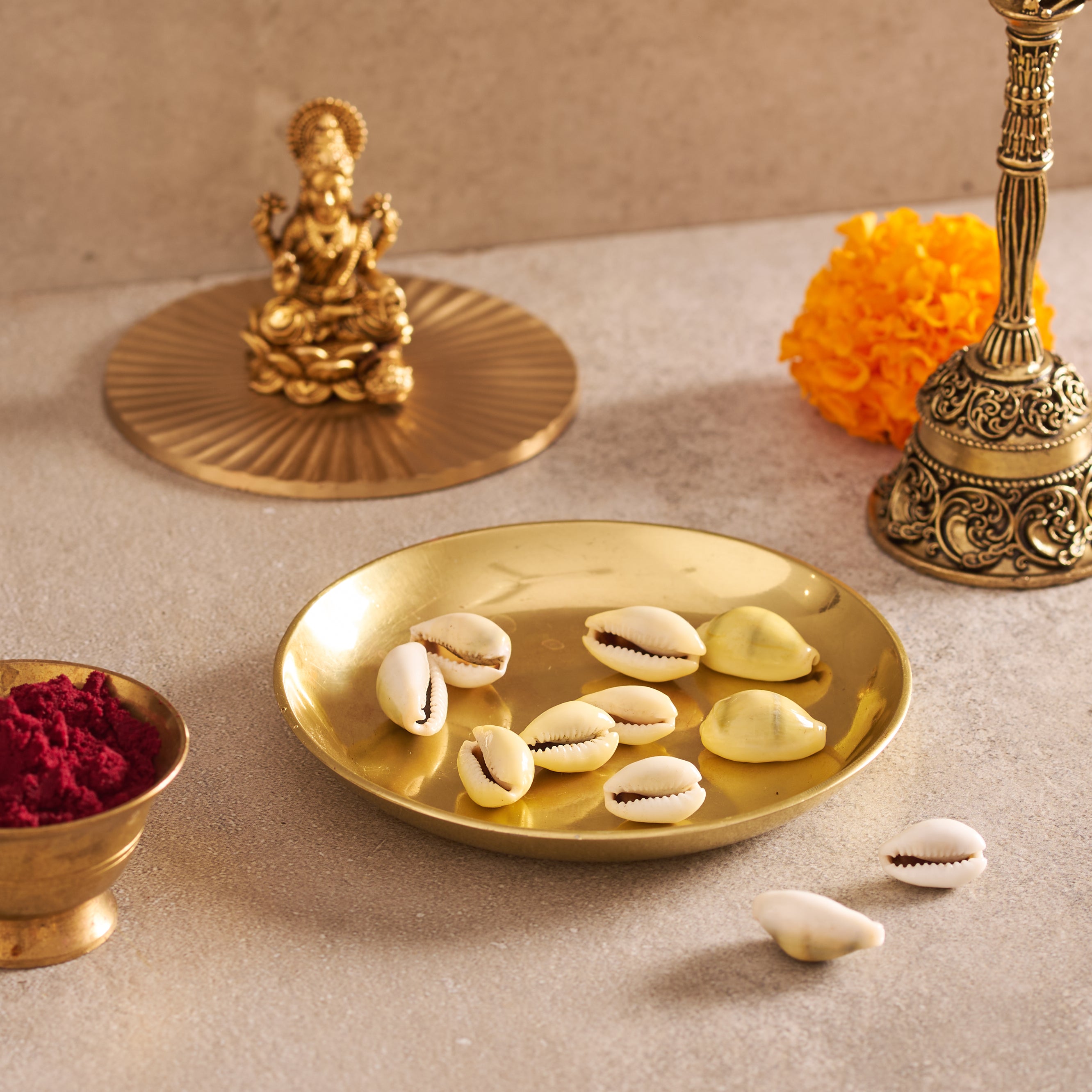 Decorative setting with gold plates, shells, and a small statue on a beige surface.