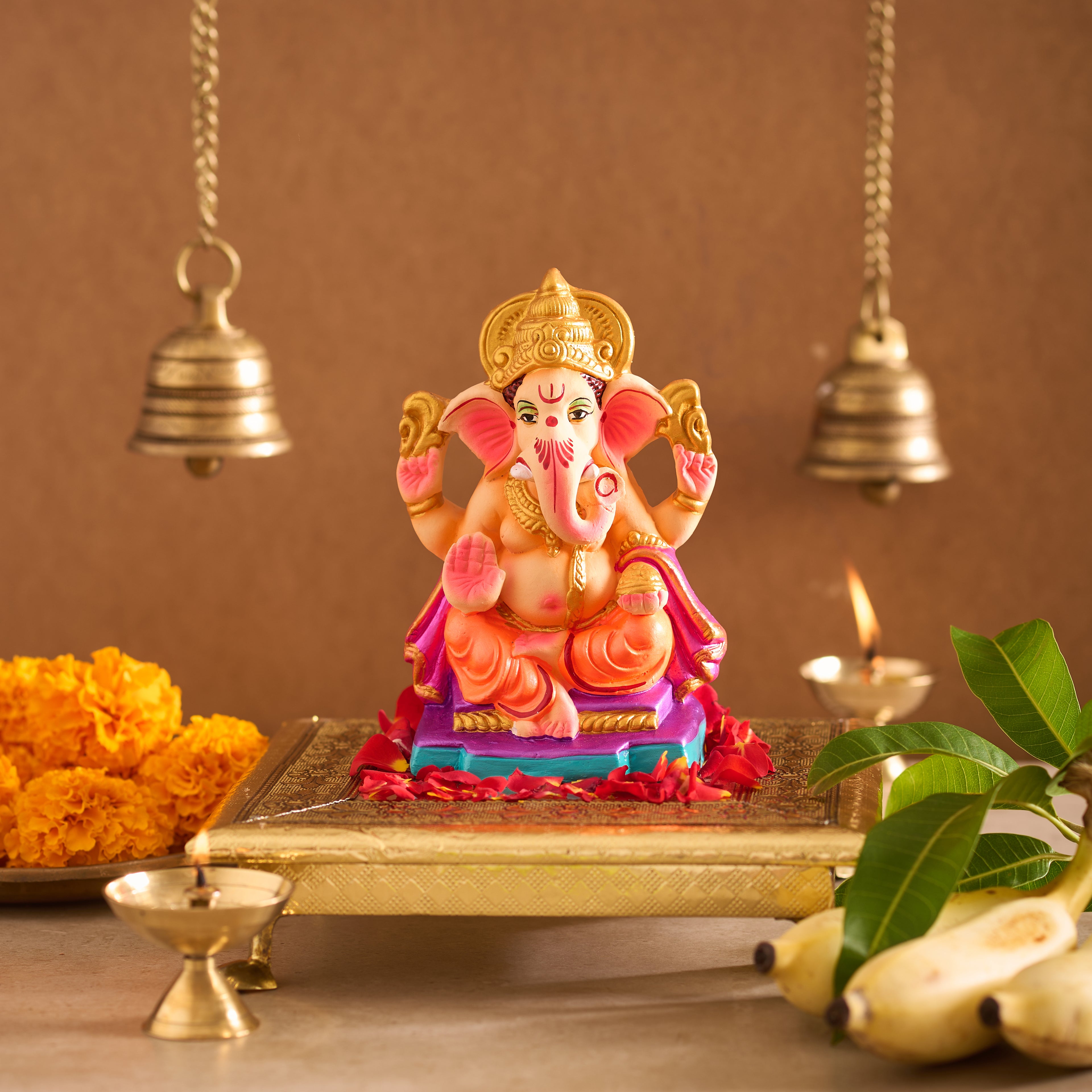 Colorful statue of a deity on a tray with marigold flowers, bells, and leaves in the background.