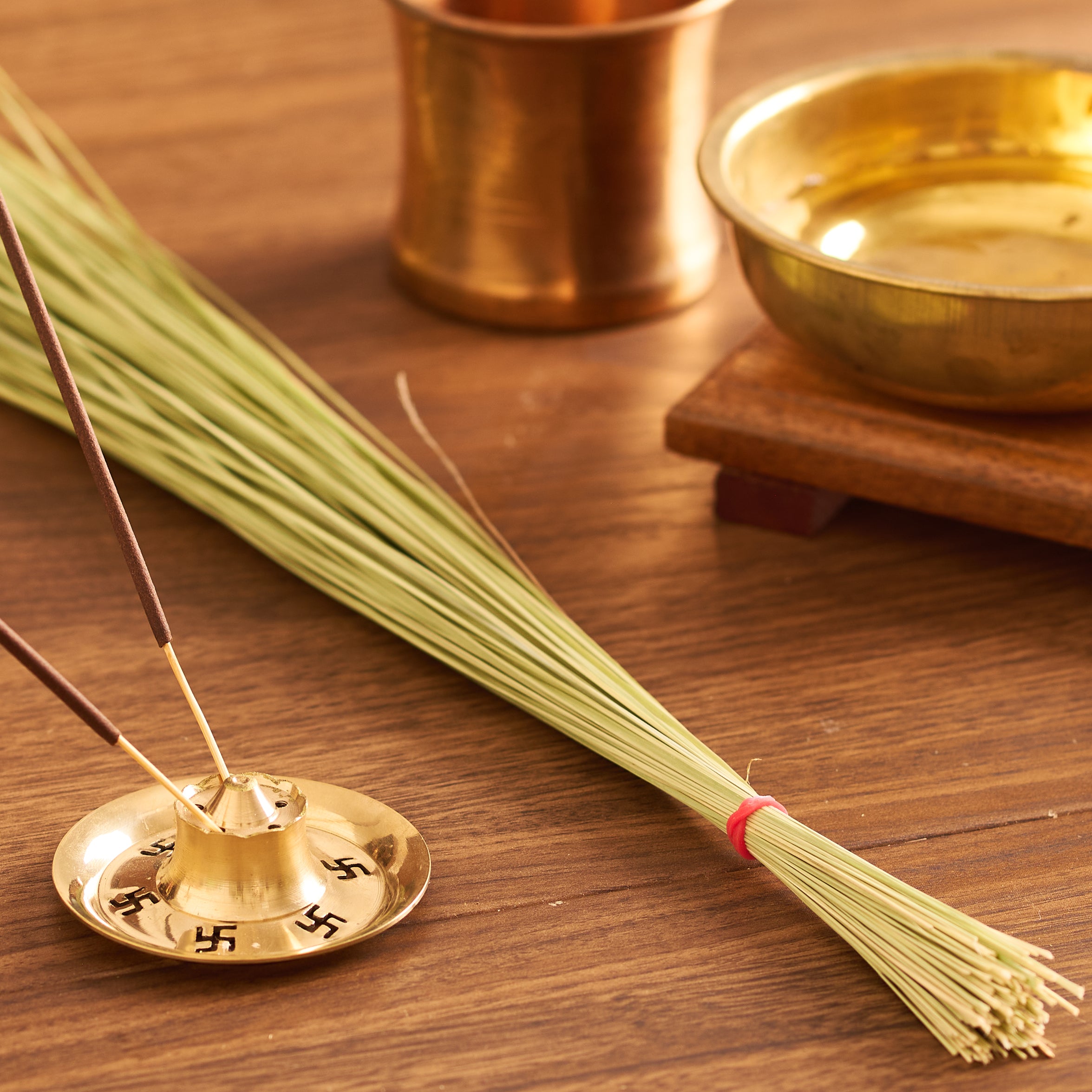 Incense stick holder with incense sticks, broom, and brass cup on a wooden surface