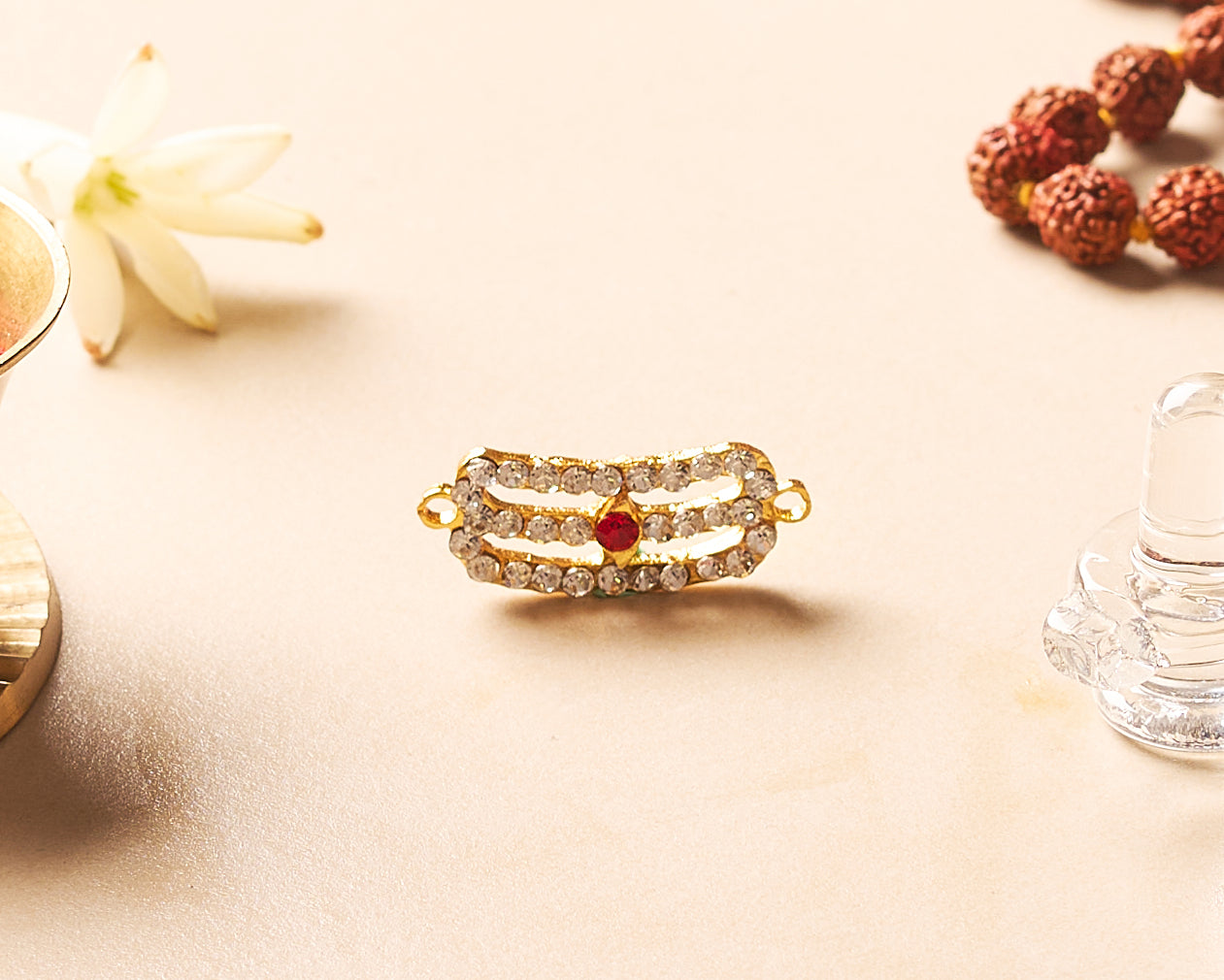 Gold bracelet with red gemstone on a beige surface with flowers and a glass.