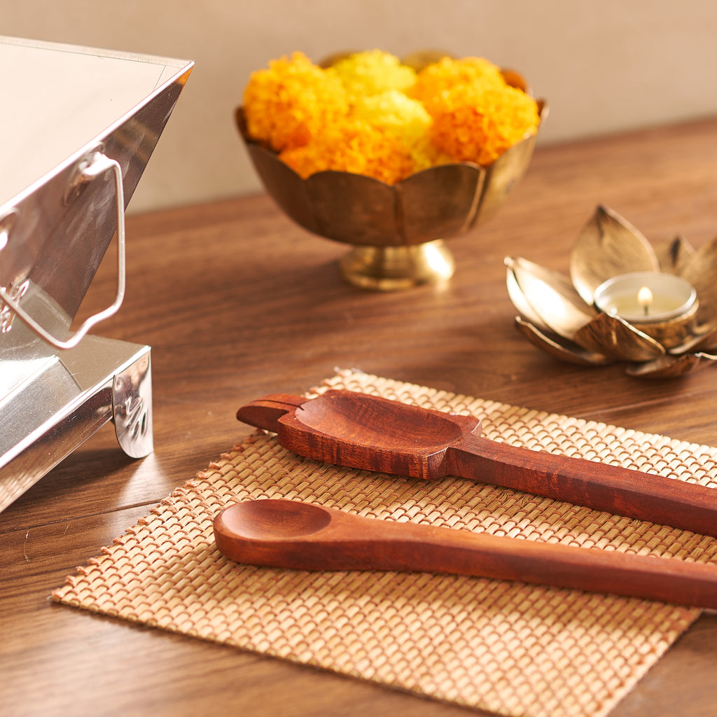 Wooden spoons on a woven mat with a bowl of marigolds in the background.