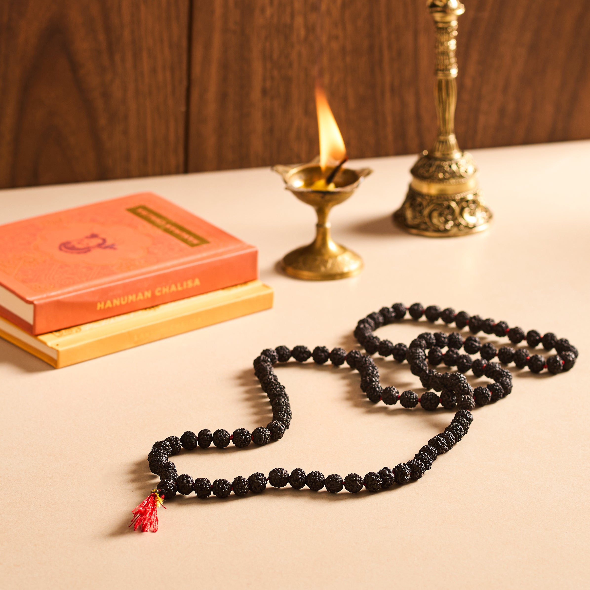 Black beaded necklace with a red tassel on a wooden surface with books and a lamp.