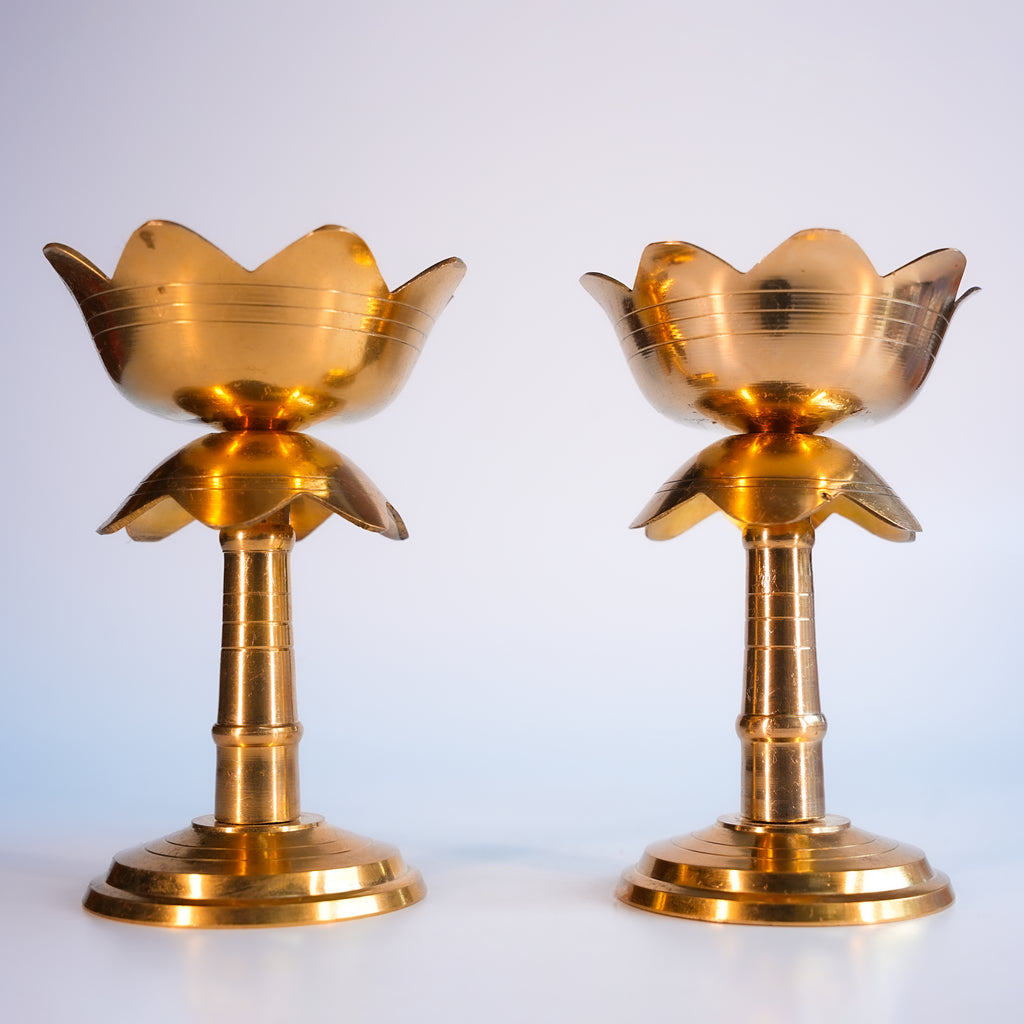 Two gold-colored lotus-shaped candle holders on a white background