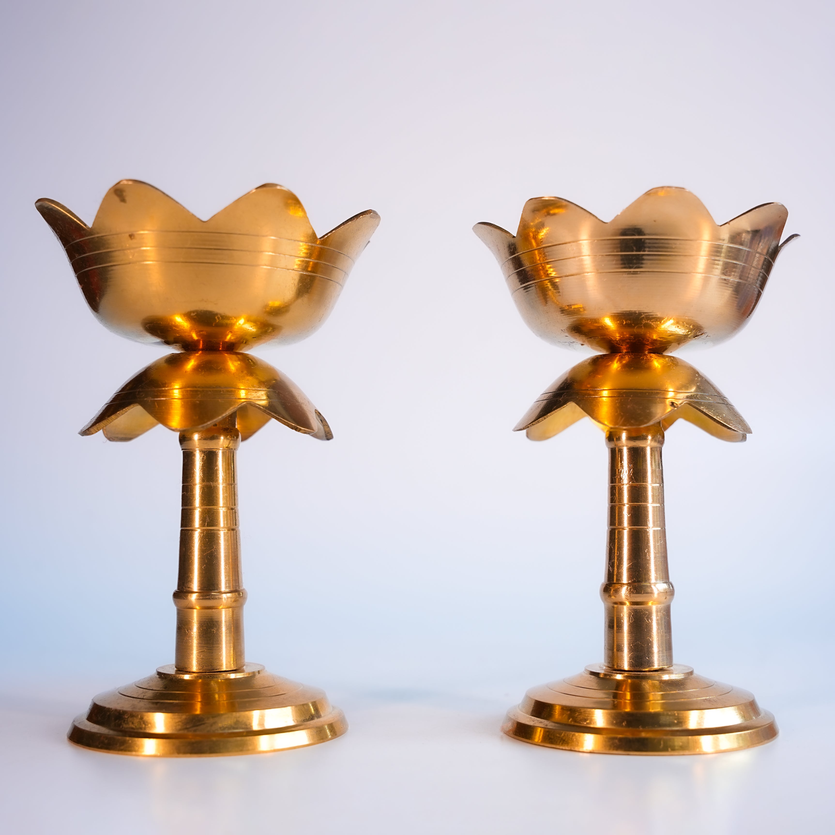 Two gold-colored lotus-shaped candle holders on a white background