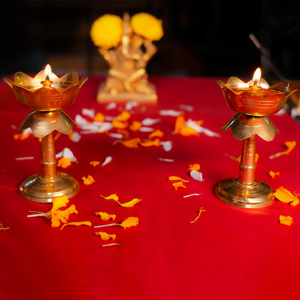 Two lit oil lamps on a red surface with yellow flowers and white petals.