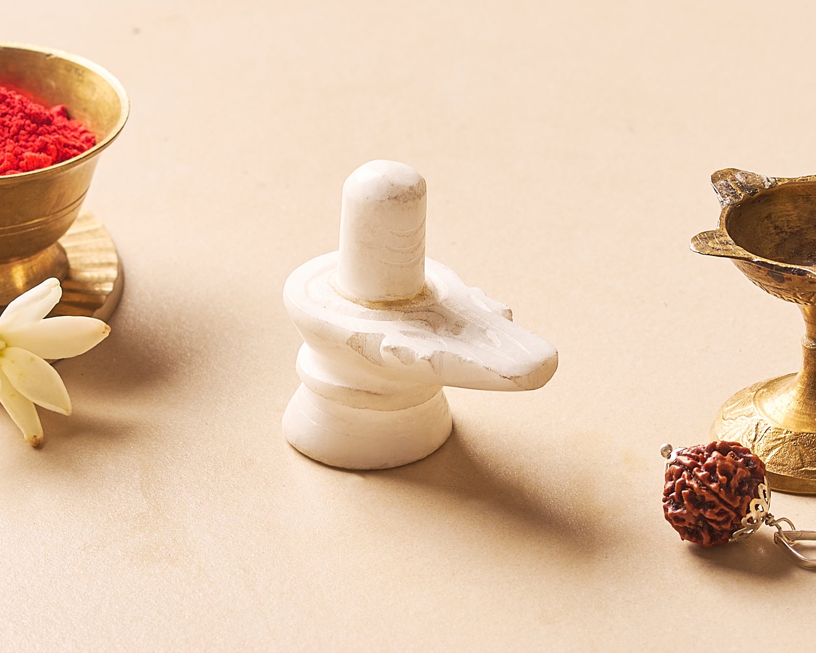White marble Shiva lingam with gold bowls and a flower on a beige background