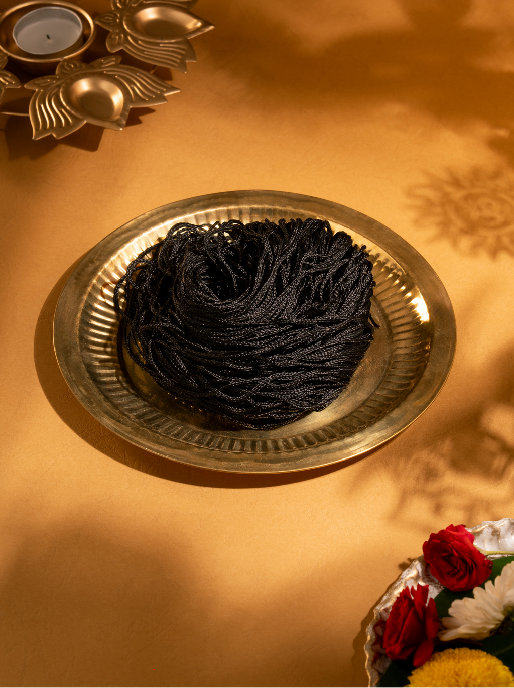Top-down view of the loose bundle of black silk thread resting next to its branded square white packaging box.