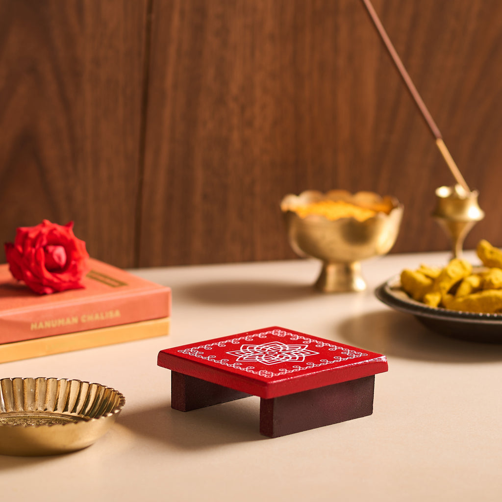 Red incense burner with gold bowls and a red flower on a wooden surface