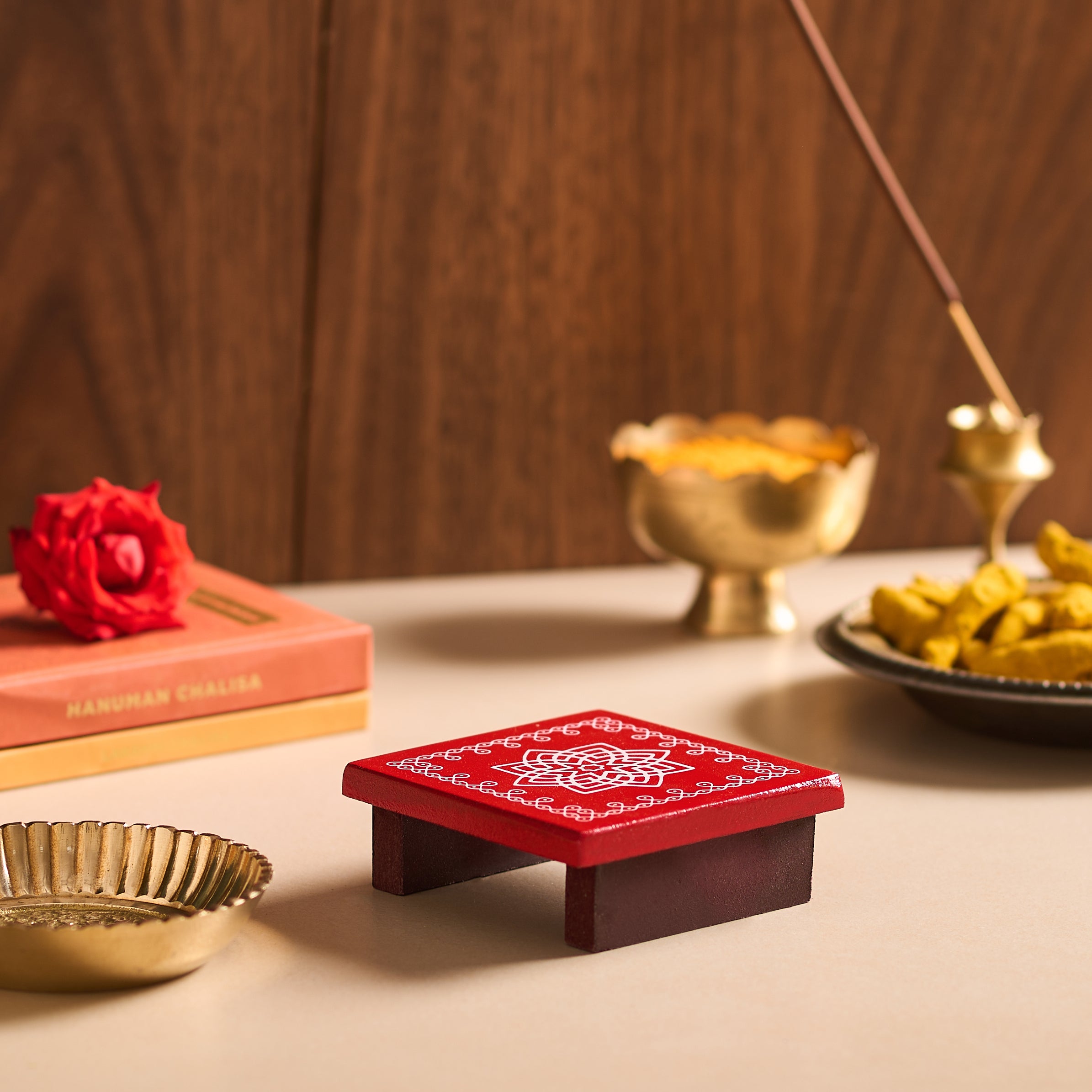 Red incense burner with gold bowls and a red flower on a wooden surface