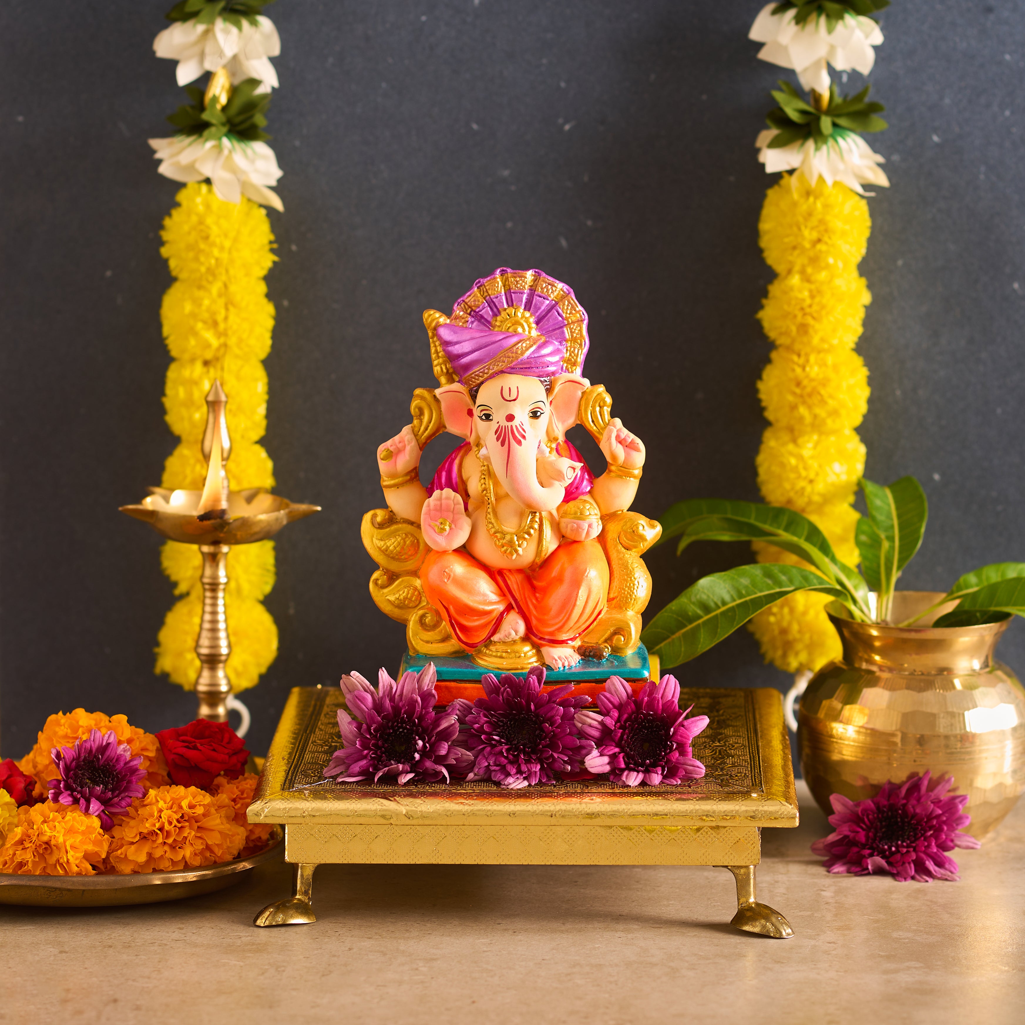 Decorative statue of a deity on a platform with flowers and lamps in the background