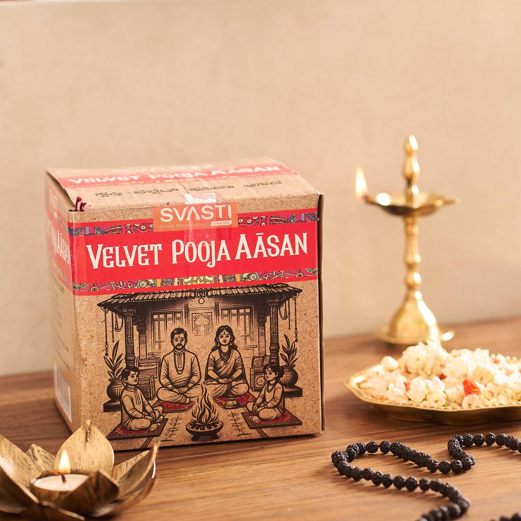 Box of 'Velvet Pooja Aasan' with candles and a plate of popcorn on a wooden surface.